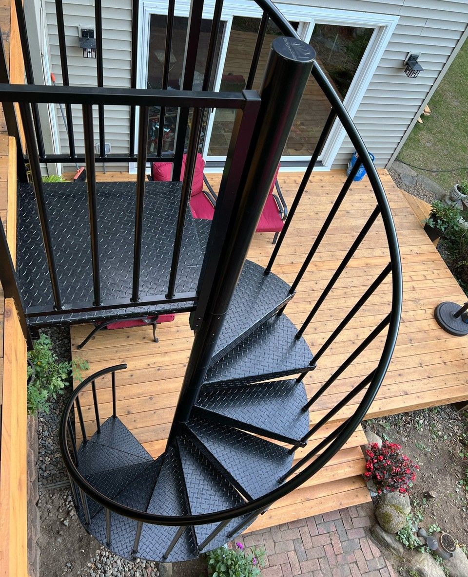 Escalier colimaçon noir à marches larmées, reliant un jardin à une terrasse en bois