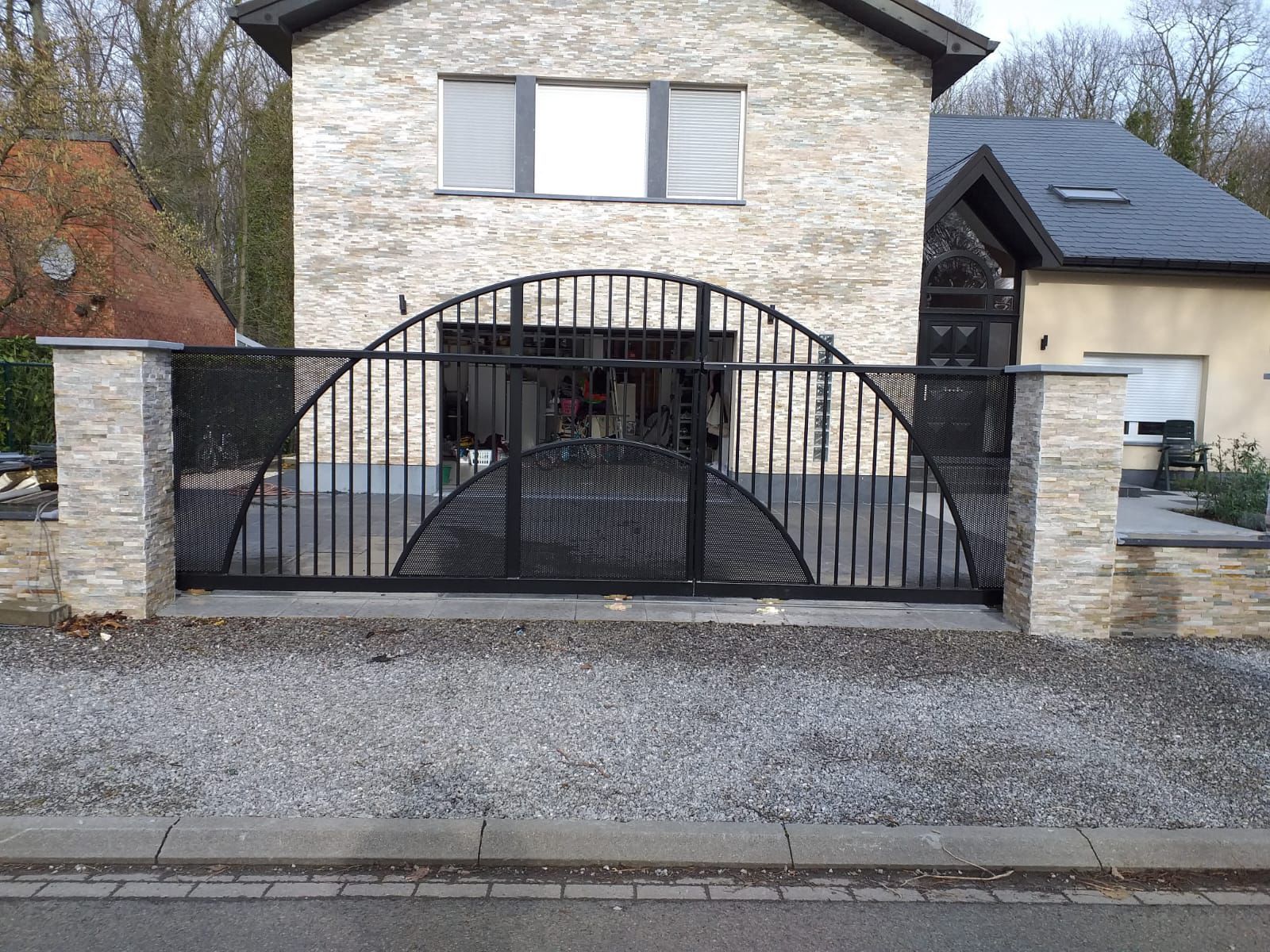 Portail noir en arche fermé entre deux piliers habillés de pierre