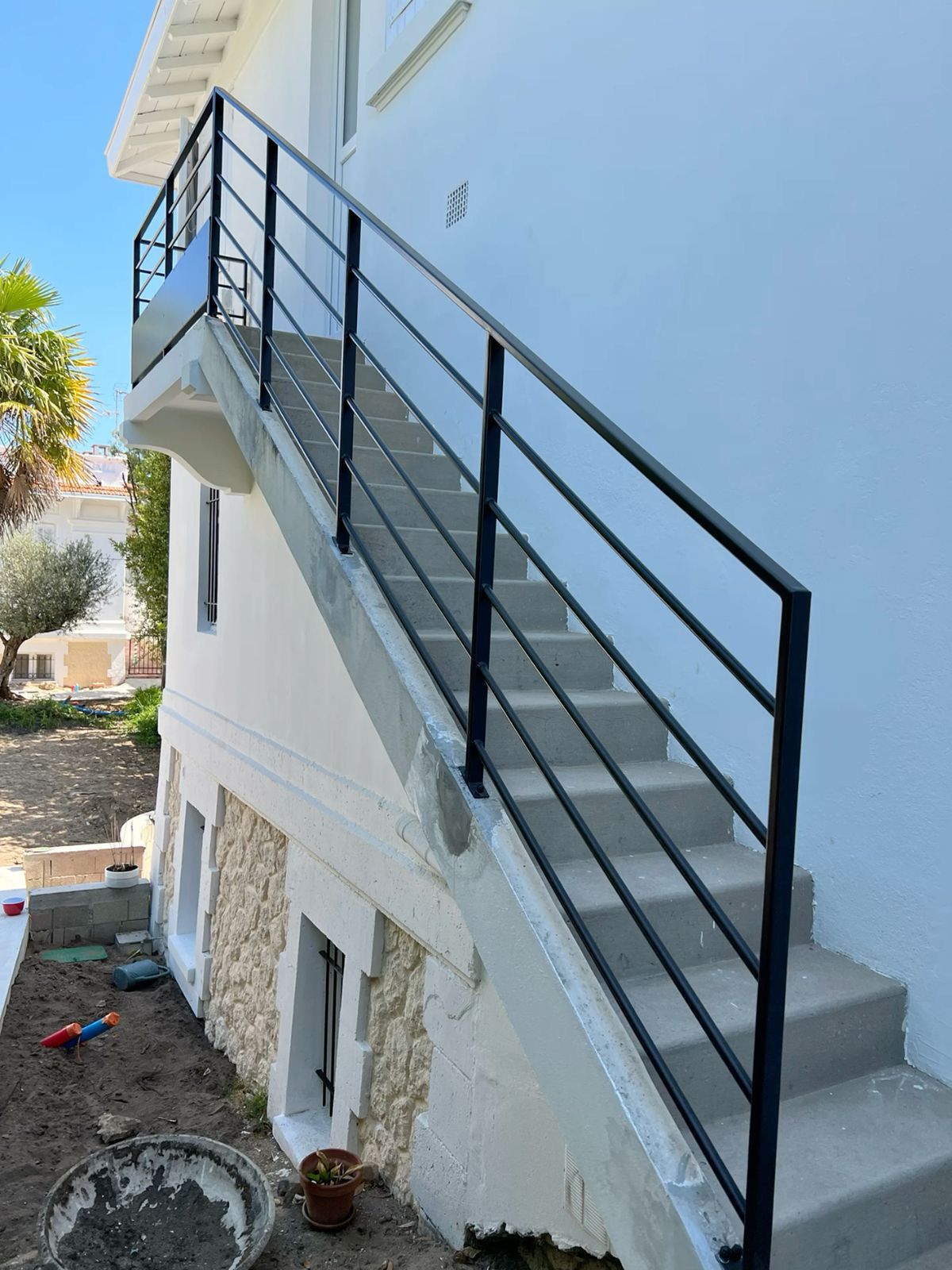 Rampe noire à lisses horizontales sur un escalier extérieur en béton